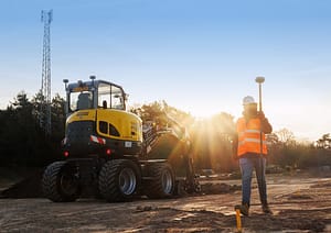 Man loopt meet digitaal in met UNI-Complete en heeft meetstok in zijn hand, linka staat een graafmachine uitgerust met UNI-Machine 3D GPS machinebesturing.